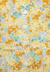 Blommig klänning med små gula, orangea och blå blommor på en vit bakgrund. Inkluderar fem vita knappar och en rynkad midja.