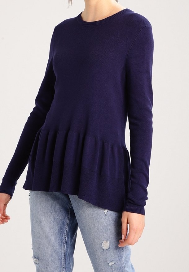 Pull bleu marine avec un col rond et des manches longues, présentant un design en peplum et des poignets côtelés. Associé à un jean délavé clair et déchiré.