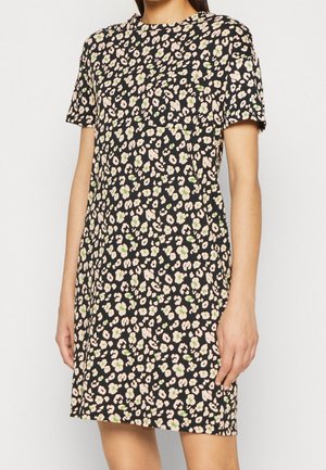 Kvinde iført en kortærmet, knælængde kjole med sort baggrund og beige og grøn floral mønster.