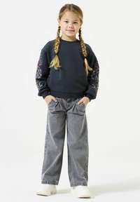 Felpa navy con ricami floreali colorati sulle maniche, abbinata a jeans grigi a gamba larga e sneakers bianche. Tessuto morbido, vestibilità comoda.