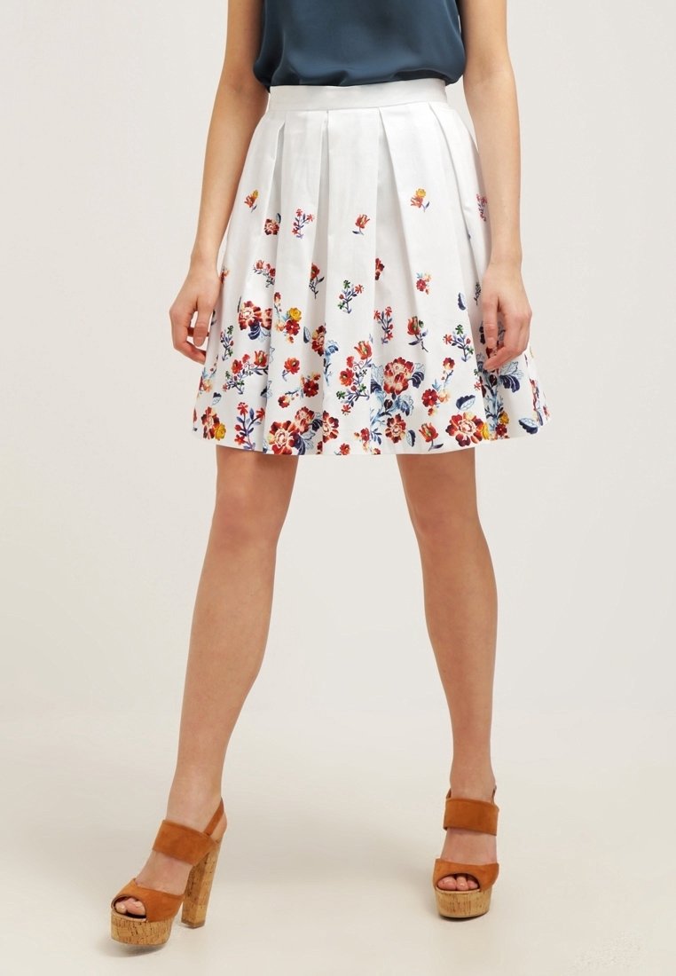 Jupe plissée blanche avec un motif floral rouge, bleu et jaune. Fabriquée en tissu léger. Dispose d'une taille ajustée.