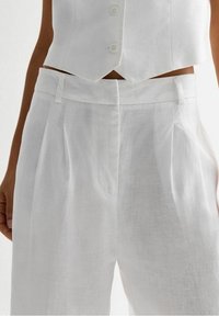 White linen pants featuring a high waist, front pleats, and side pockets. The fabric has a textured, breathable appearance.