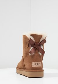 Hnedé semišové ankle boots s umelým kožúškom a dekoratívnou hnedou mašľou na zadnej strane. Obsahujú gumovú podrážku a embosované logo značky.