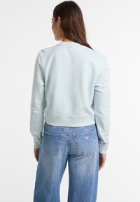 Lichtblauwe cropped sweatshirt met geribbelde manchetten en zoom, gecombineerd met high-waisted denim jeans met een klein logo label op de achterzak.