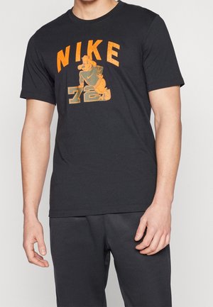 T-shirt noir Nike avec le texte "NIKE" en orange, un chien caricatural portant une casquette et une veste, et le numéro "78" en dessous du chien.