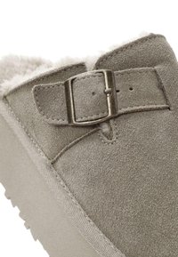 Scarpa slip-on in suede grigio con suola sintetica, caratterizzata da un accento di fibbia metallica e un morbido rivestimento in pelliccia sul colletto per il massimo comfort.