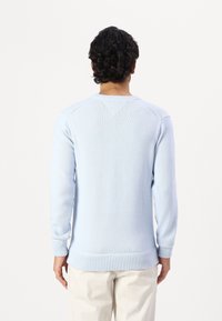 Pull en tricot bleu clair avec des manches longues, poignets et ourlet côtelés, comprenant un détail de couture en V dans le dos. Texture douce et design ajusté.