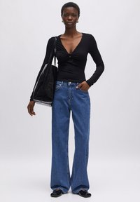 Zwarte lange mouw top met een gedraaide halsontwerp, gecombineerd met lichtblauwe wijde jeans. Een zwarte tote tas en glanzende zwarte schoenen maken de uitstraling compleet.