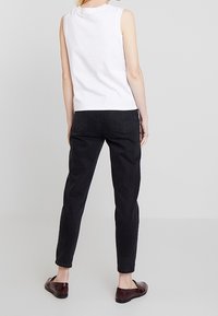 Biała bezrękawnik połączona z czarnymi zwężającymi się dżinsami i brązowymi butami. Czysty design z minimalnymi detalami. Gładka tekstura materiału.