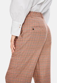 Karo-Hosen mit hoher Taille in Orange- und Brauntönen mit blauen Akzenten. Verfügt über seitliche Taschen und eine Gesäßtasche mit einem Knopf.