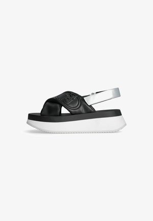 Sandales plateforme synthétiques noires avec une large sangle texturée et des accents argentés, présentant une épaisse semelle extérieure blanche avec un motif en zigzag.