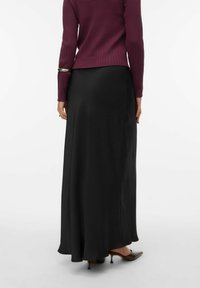 Zwarte, jurk tot de vloer met een gladde textuur en een uitlopende zoom. Gecombineerd met een bordeauxrode geribbelde trui met lange mouwen.