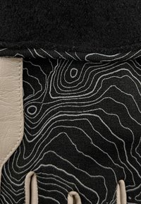Tissu noir présentant un motif topographique en lignes blanches, avec une accent en cuir texturé beige et un superposé en feutre noir en haut.