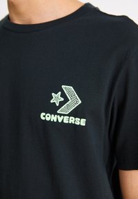 Black cotton t-shirt with a crew neck, featuring a light green Converse logo and graphic design on the chest.