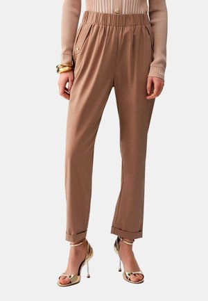 Pantaloni marroni a vita alta con gamba affusolata e orli risvoltati, dettagli con bottoni dorati sulle tasche, indossati con sandali dorati con tacco alto e top beige a coste.