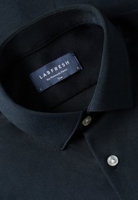 Slankpassende donkerblauwe polo met structuurstof, een puntkraag en een knoopsluiting met drie knopen. Bevat een label met "LABFRESH" branding.