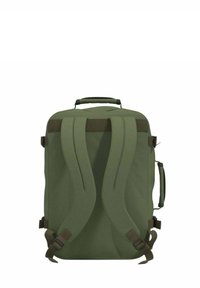 Vihreä kangasreppu, jossa on kaksi pehmustettua olkahihnaa, ylätassu ja säädettävät sivuhiulut; minimalistinen muotoilu ja sileä pinta.