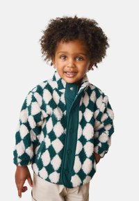 Veste en polaire avec un motif en losanges teal et blanc, dotée d'une fermeture avant contrastée en teal et d'une finition douce et texturée.