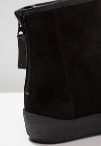 Botte de cheville en suède noir avec une semelle en caoutchouc noir texturé, fermeture éclair sur le côté et un design minimaliste ; présente des coutures soignées le long des coutures.