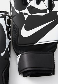Black and white Nike gloves with a geometric pattern, textured grip, and Velcro strap, showcasing a distinctive logo.