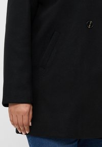 Cappotto in lana nera con chiusura a singolo bottone, tasca laterale e tessuto texture. Maniche a cappotto e design a taglio dritto.