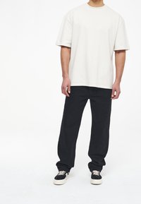 Krémové oversized tričko v kombinaci s černými rovnými kalhotami. Boty jsou černé tenisky s bílou podrážkou a tkaničkami. Minimalistický design.