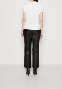 Camiseta blanca de manga corta combinada con pantalones anchos de cuero negro de tiro alto y zapatos de tacón negro, vista desde atrás.