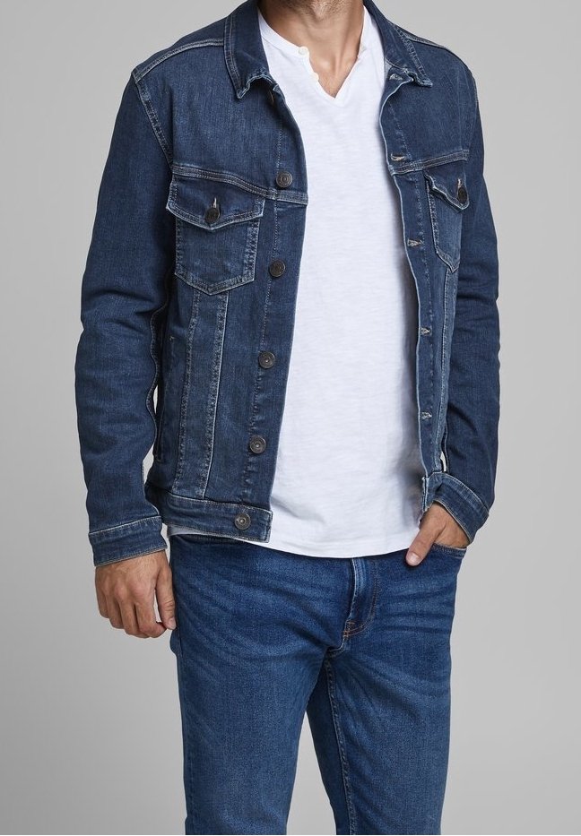 Denim jacket in dark blue with two chest pockets and contrasting button closures. Worn over a white v-neck t-shirt and paired with blue jeans.