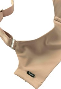 Soutien-gorge in tessuto elasticizzato beige con una superficie liscia, spalline regolabili e un'etichetta nera sul lato. Design semplice e senza cuciture.