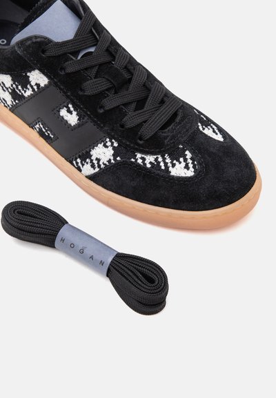 Baskets en daim noir avec des détails blancs à motifs, semelle en gomme, lacets noirs et une paire supplémentaire de lacets noirs étiquetés Hogan sur une bande grise.