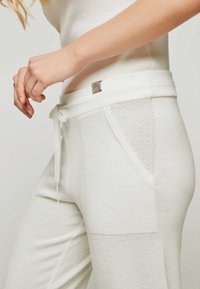 Weiße, lässige Hose mit einem gerippten Taillenbund, zwei Seitentaschen, strukturierten Stoffakzenten und einem gebundenen Kordelzug. Verfügt über ein kleines Logo-Tag.