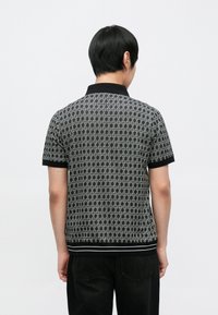 Polo de manga curta em preto e cinza com padrão geométrico, gola com colarinho e acabamento preto nas mangas e na barra.