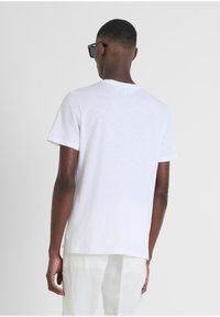 Camiseta blanca de manga corta con cuello redondo, que presenta un corte relajado, textura suave y aberturas laterales. Combinada con pantalones de color crema.
