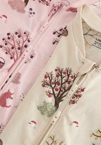 Zwei Kinder-Jumpsuits mit Reißverschluss: einer in hellrosa mit Bäumen und Tieren, der andere in creme mit Apfelbäumen und Pilzen. Weicher Stoff.