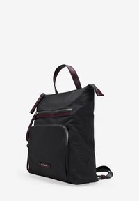 Mochila de tela negra con detalles de cuero burdeos, que cuenta con varios bolsillos con cremallera, forma plana y correas ajustables.
