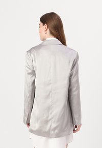 Lys grå satengblazer med en skreddersydd design, med klaffelapp og forlenget bakdel. Har lange ermer og en glatt tekstur.