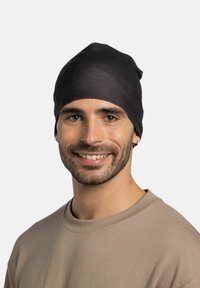 Black beanie hat made of soft fabric, featuring a snug fit and smooth texture, worn by a person with a light brown shirt.