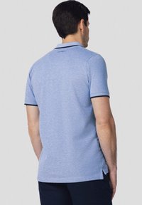 Jasnoniebieska koszulka polo z krótkimi rękawami, kontrastowe ciemne mankiety oraz boczne rozcięcia. Miękka tkanina o subtelnej fakturze, logo przy szyi.