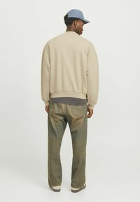Beige sweatshirt with dropped shoulders, ribbed cuffs, and hem, paired with faded blue jeans and a light blue cap. Casual fit.