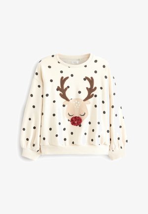 Barn iført hvid sweater med prikker og rensdyrmotiver, sorte lædershorts, sorte strømpebukser og sorte knæhøje støvler, løfter det ene ben.