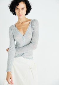 Lichtgrijze cardigan met lange mouwen, een diepe V-hals, kantafwerking en knoopsluiting. De gestructureerde stof contrasteert met een gladde, off-white rok.