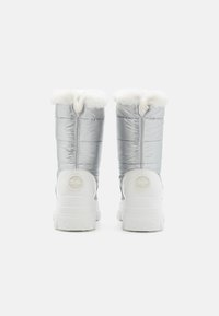 Water-resistant silver puffer boots with faux fur trim, quilted design, and white rubber soles. Features a circular logo on the heel.