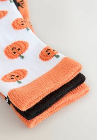 Drei Paar Socken: ein weißes Paar mit orangefarbenen Kürbis-Prints, ein orangenes Paar und ein schwarzes Paar. Alle haben eine gerippte Textur und kontrastierende Bündchen.