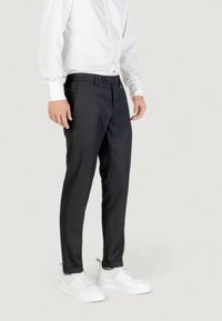 Pantalones negros ajustados con una textura suave, con un frente plano, bolsillos laterales y un cinturón. Combinados con zapatillas blancas y una camisa blanca.