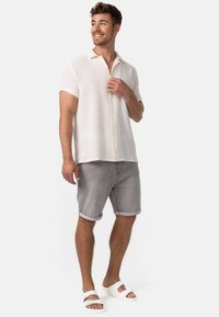 Chemise blanche à manches courtes et col, en tissu texturé, associée à un short gris clair retroussé et des sandales blanches. Comprend des boutons et une coupe décontractée.