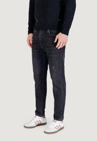 Jeans in denim scuro con vestibilità slim, caratterizzati da una leggera scoloritura e dettagli strappati. Abbinati a sneakers bianche con accenti marroni.