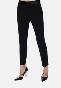 Pantaloni neri su misura con vestibilità slim, dotati di una cintura liscia e lucida e di una chiusura a bottone. Abbinati a tacchi a punta neri.