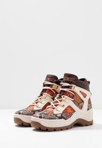 Wysokie sneakersy z brązowym, pomarańczowym i beżowym wzorem w węża, białymi sznurowadłami, złotymi oczkami i grubymi brązowymi gumowymi podeszwami.