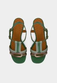 Πράσινα και γκρι δερμάτινα σανδάλια με επίπεδη σόλα, που διαθέτουν μεταλλικές λεπτομέρειες και ρυθμιζόμενο λουράκι, παρουσιάζοντας έναν μίνιμαλ σχεδιασμό.