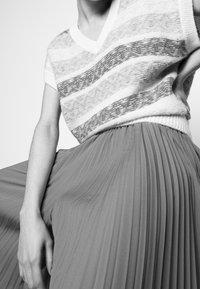 Neulepaita V-pääntiellä, jossa on vaaleanharmaita raitoja. Yhdistetty virtaavaan, laskostettuun midi-hameeseen, joka on syvässä tiilenpunaisessa sävyssä.